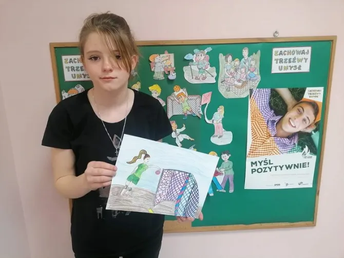 Na zdjęciu uczestniczka konkursu plastycznego pt. „Nie czas na nudę" przedstawia swoją pracę plastyczną