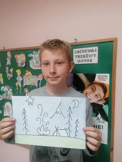 Na zdjęciu uczestnik konkursu plastycznego pt. „Nie czas na nudę" przedstawia swoją pracę plastyczną