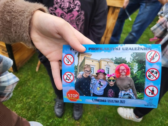 Na zdjęciu osoba pokazuje wykonane zdjęcie w fotobudce, na którym znajduje się czworo uczestników festynu